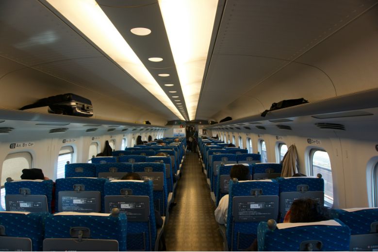 The inside of a Japanese Shinkansen (Bullet train), several rows of blue seats in a 3-2 configuration.