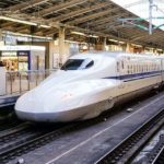 While Shinkansen (bullet train) with a blue stripe on the side at a train platform. Train Etiquette.