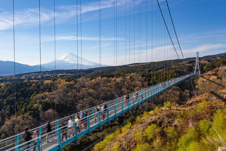 The glass bridge of Mishima skywalk with a snow covered Mt. Fuji behind.