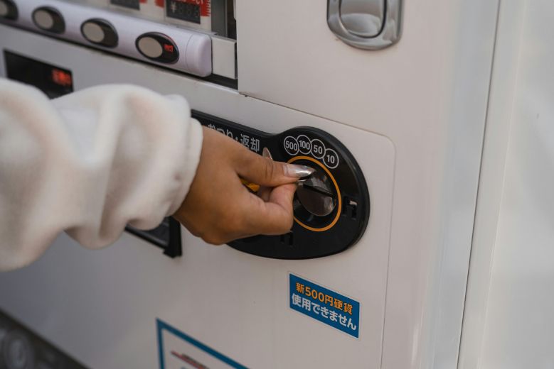 A hand inserting coins into a Japanese vending machine.